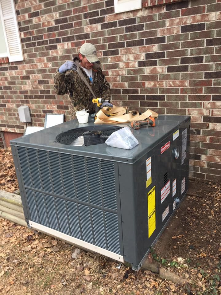 Technician finishing a new package unit installation beside a brick home